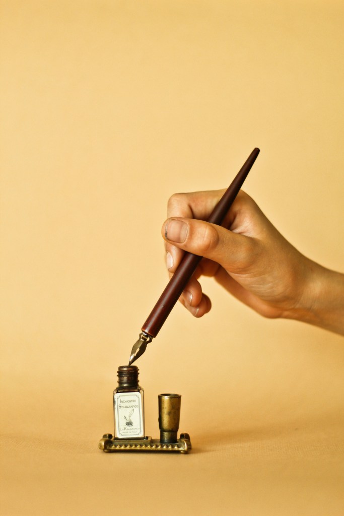 A hand holding a pen over an inkpot